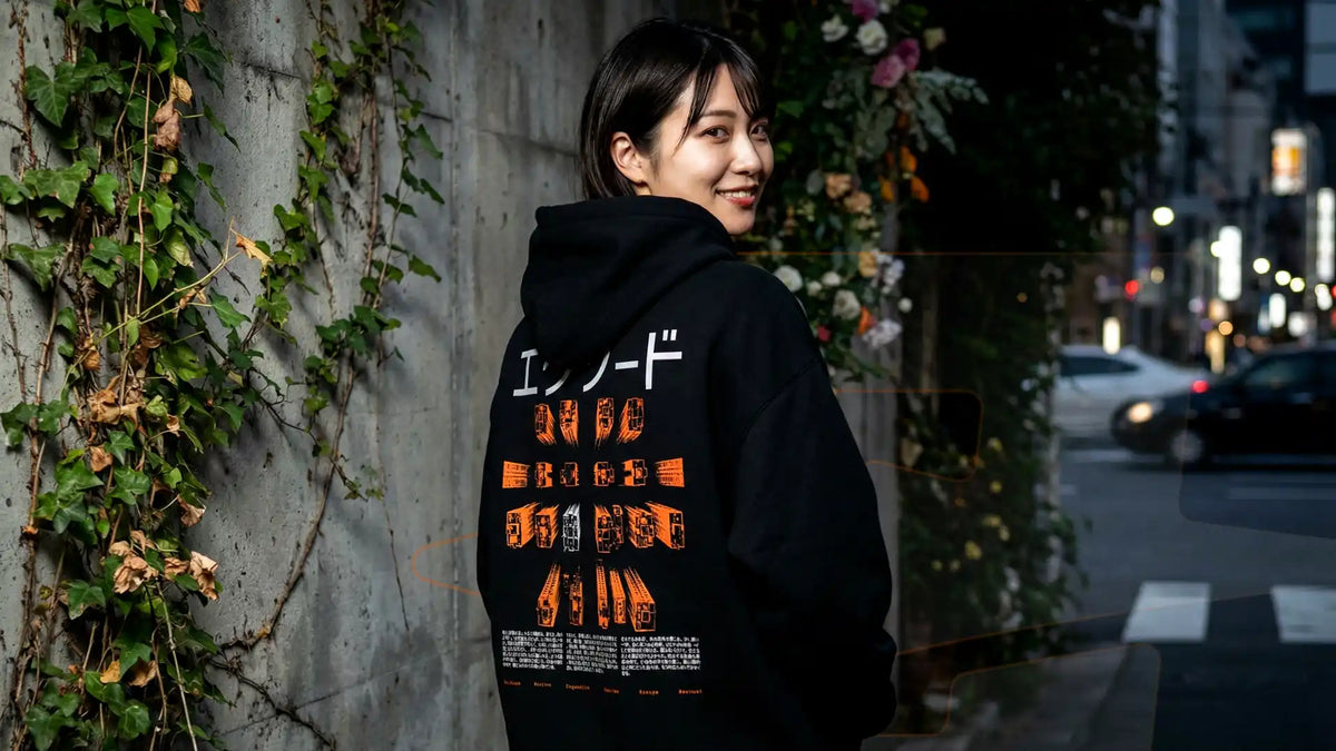 Femme souriante vue de dos en hoodie oversize EXODE CORPORATE noir, grille de pictogrammes orange, de nuit en ville